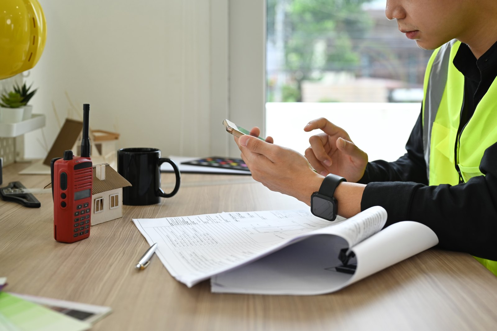 Worker in a high-visibility vest using a phone beside paperwork